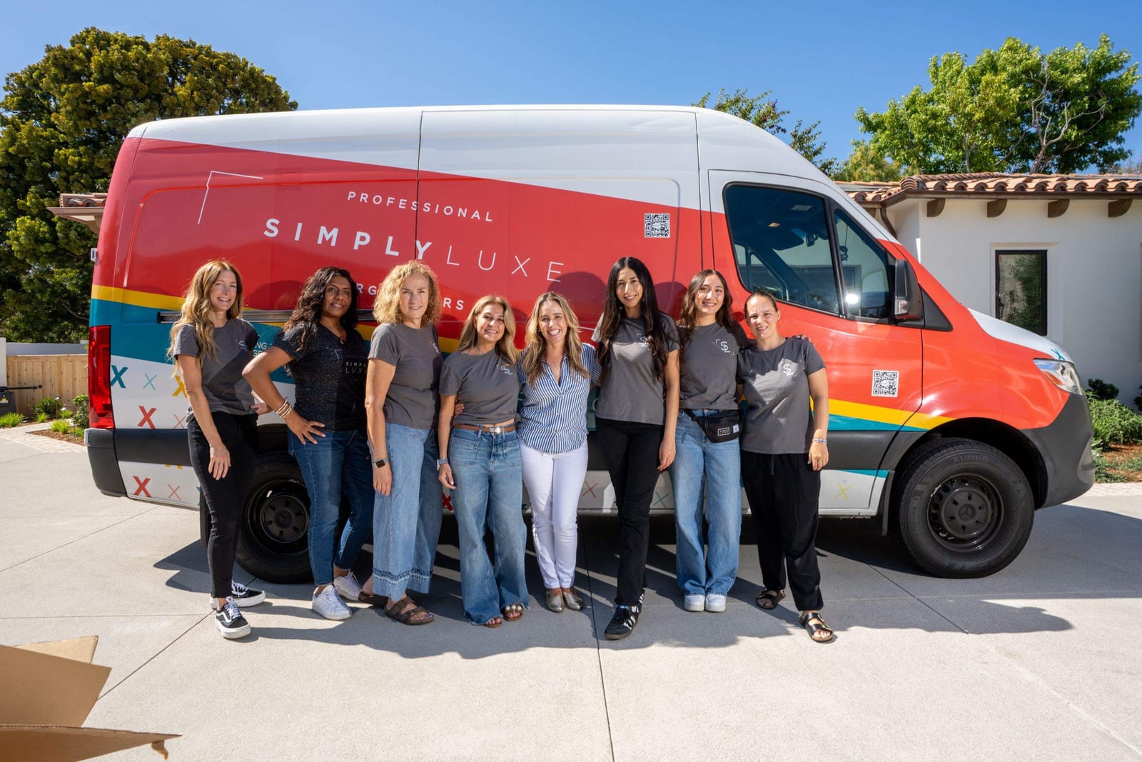 The Simply Luxe team of eight standing together in front of their branded red and white van