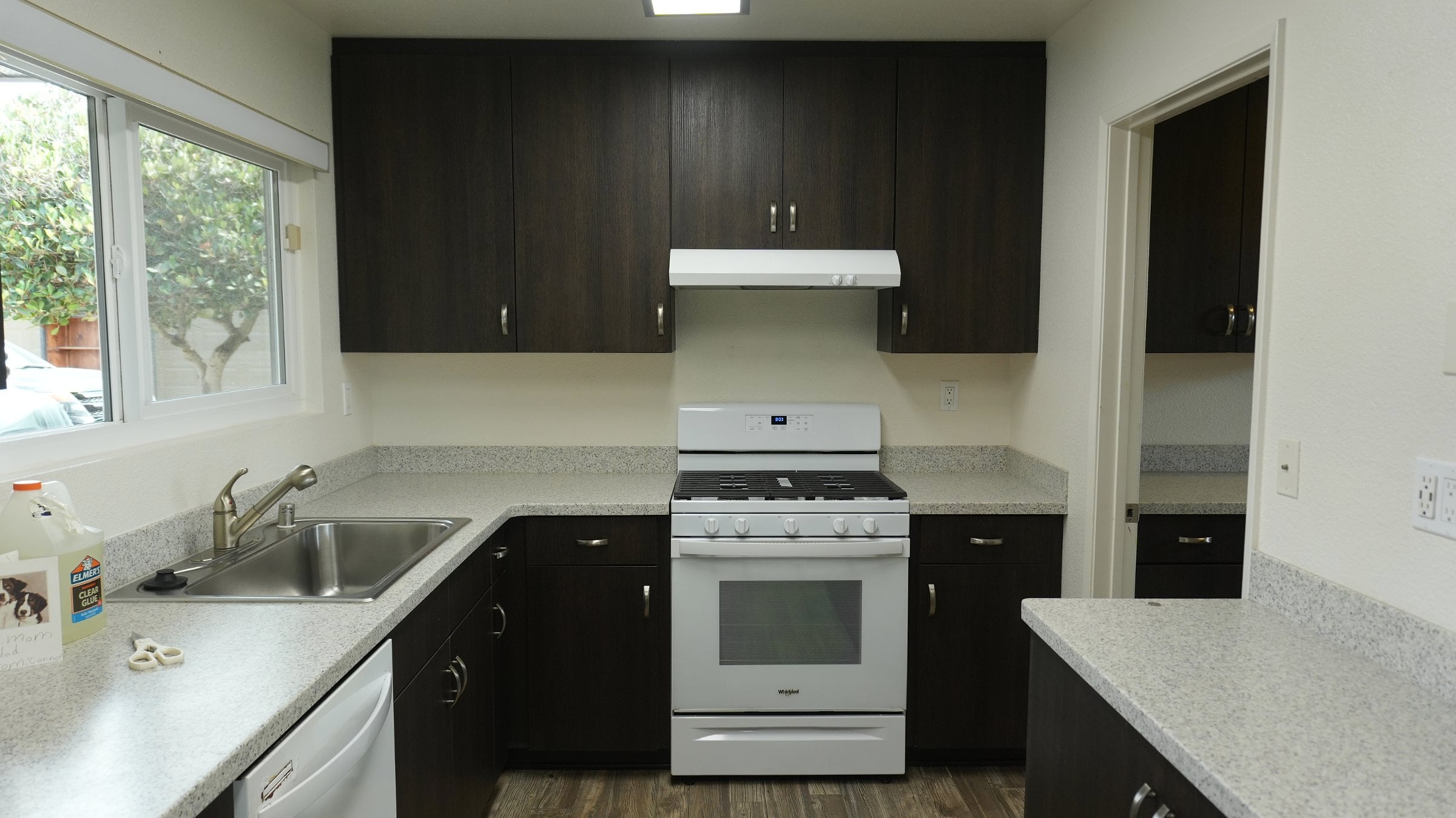 Kitchen with dark brown cabinets, gray speckled countertops, a white gas range with hood, and a stainless steel sink near a window