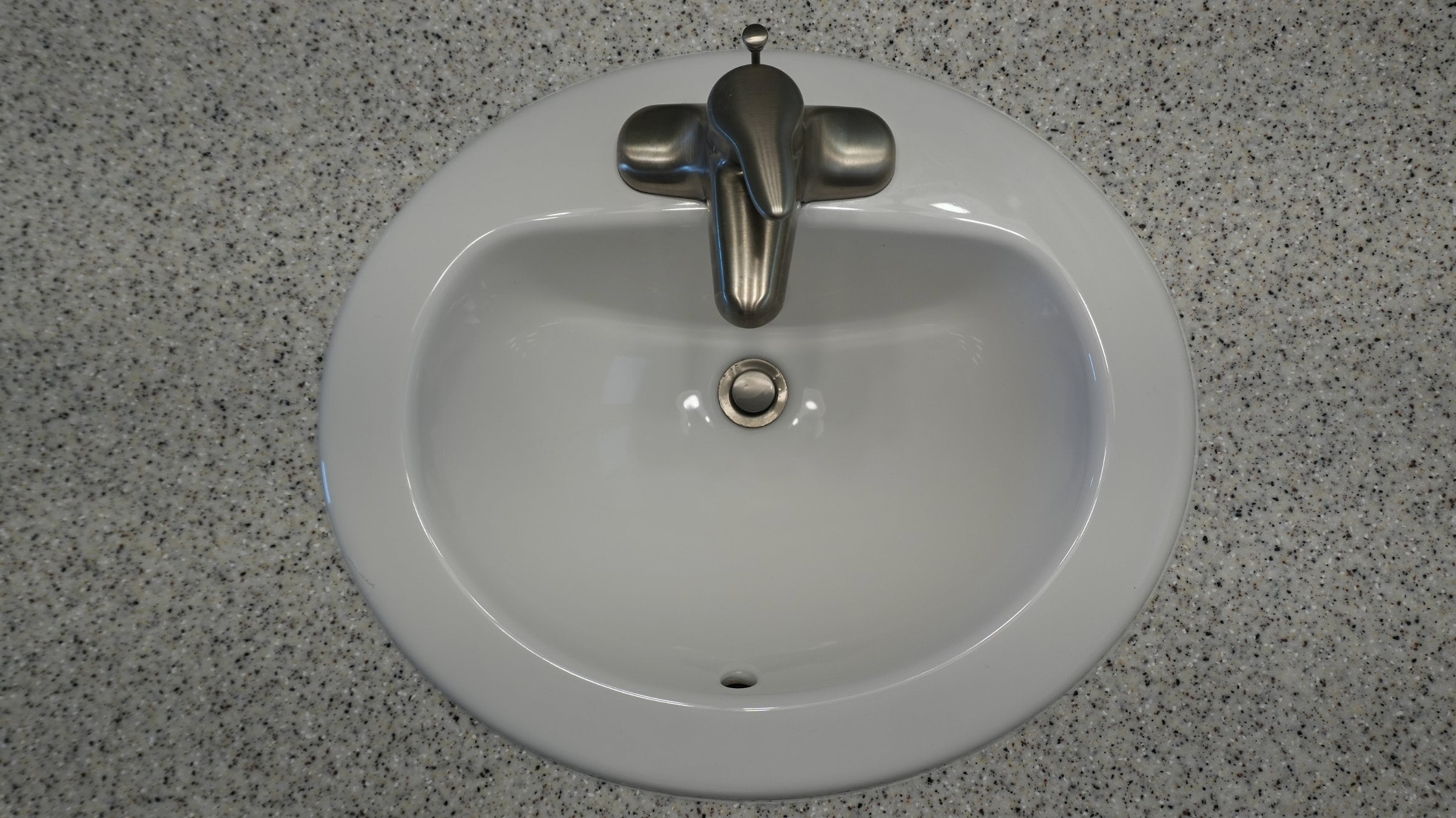 Overhead view of a clean white oval bathroom sink with a brushed-nickel faucet set in a gray speckled countertop
