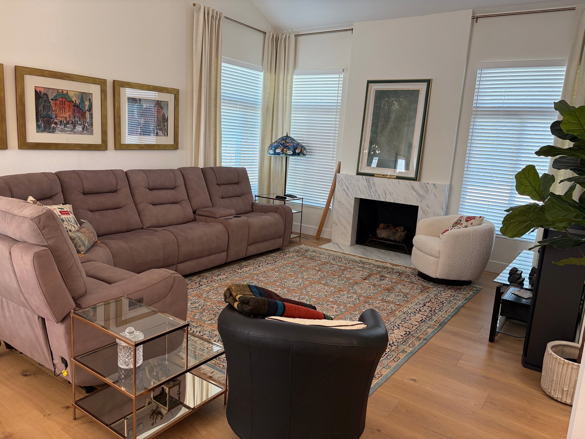 A living room with a large gray sectional sofa, patterned area rug, marble fireplace, and hardwood floors