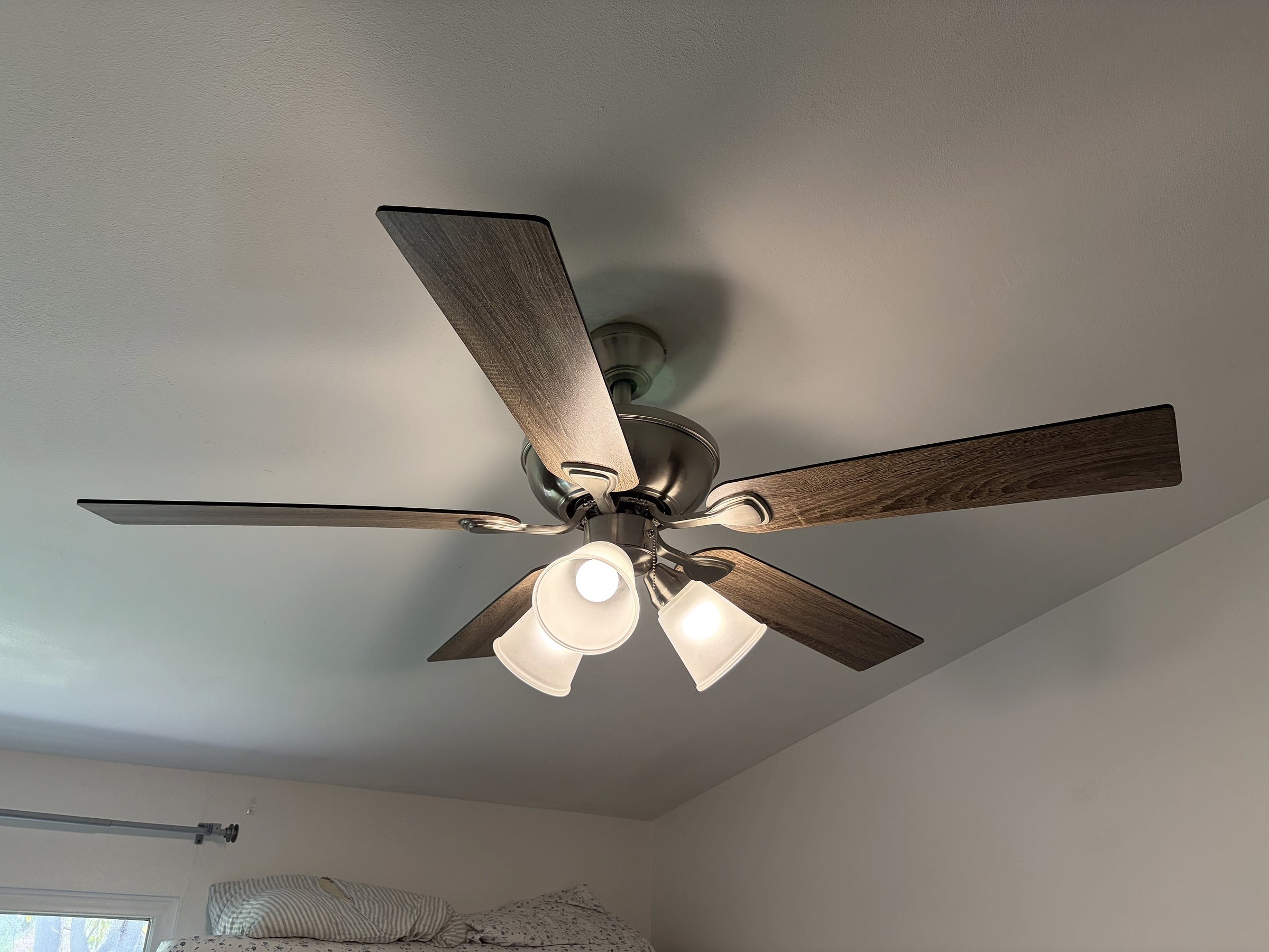 Five-blade wood-tone ceiling fan with brushed nickel hardware and three lit frosted glass light shades mounted on a white ceiling