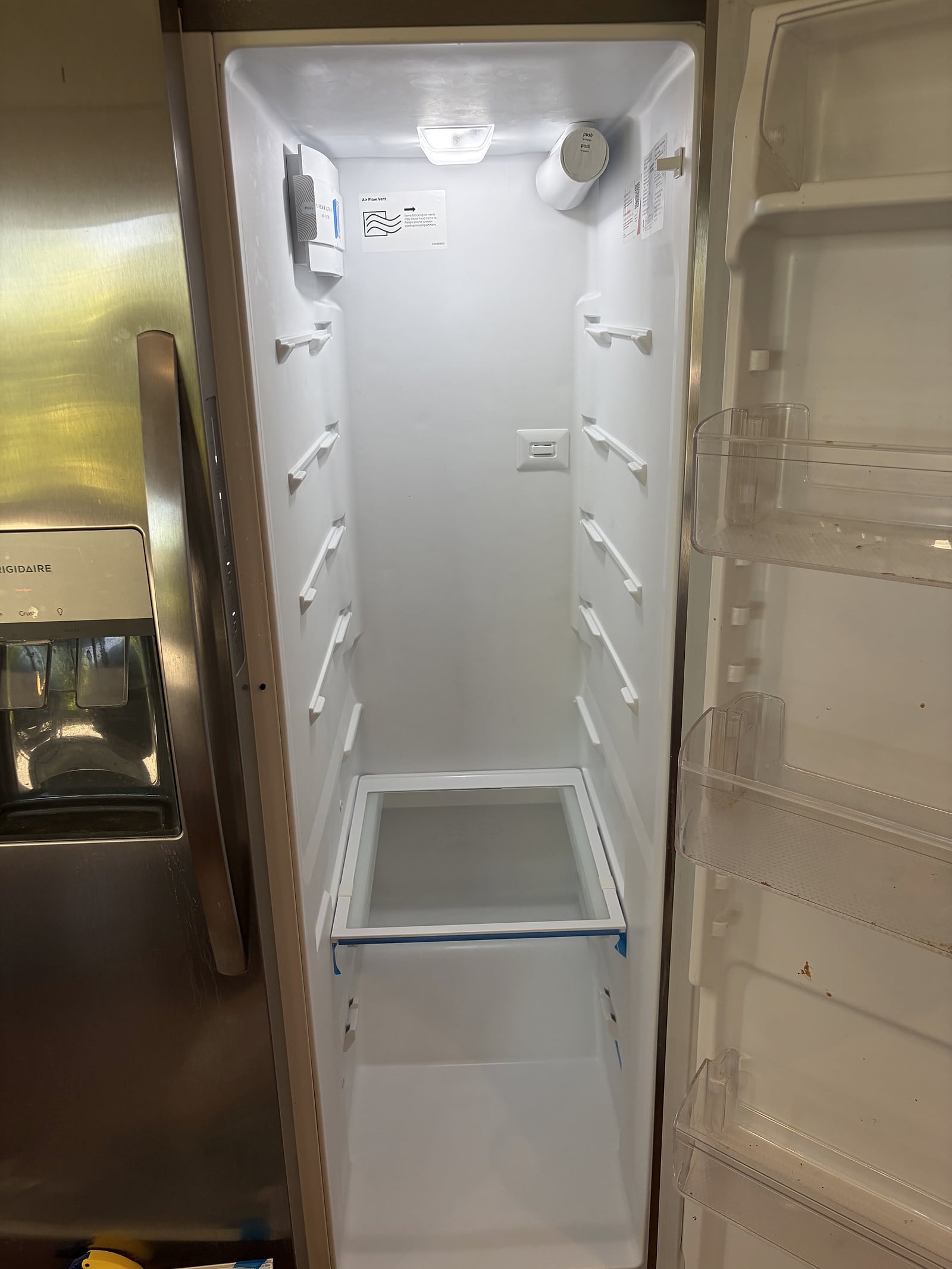 Open, empty Frigidaire side-by-side refrigerator compartment with white interior shelves and lit interior light