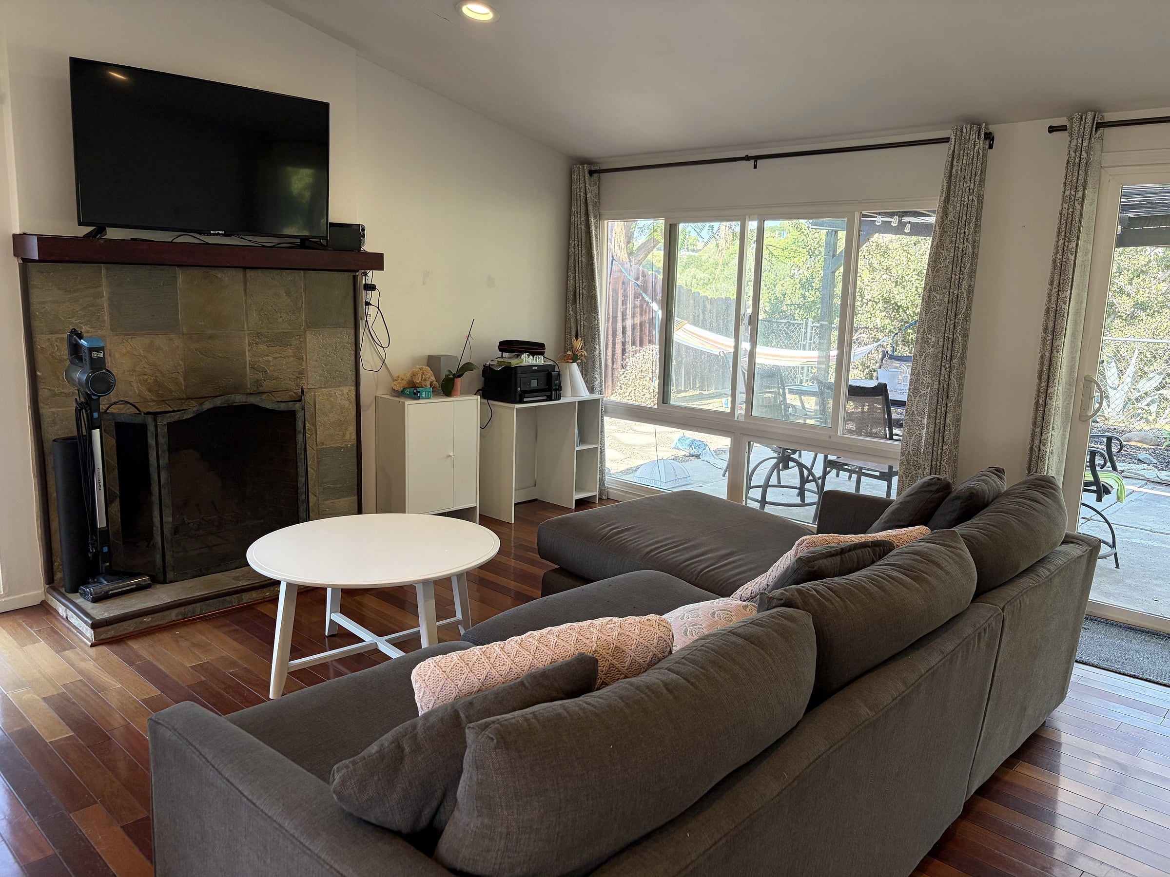 Living room with a gray sectional sofa, white round coffee table, stone fireplace with wall-mounted TV, and large sliding glass doors
