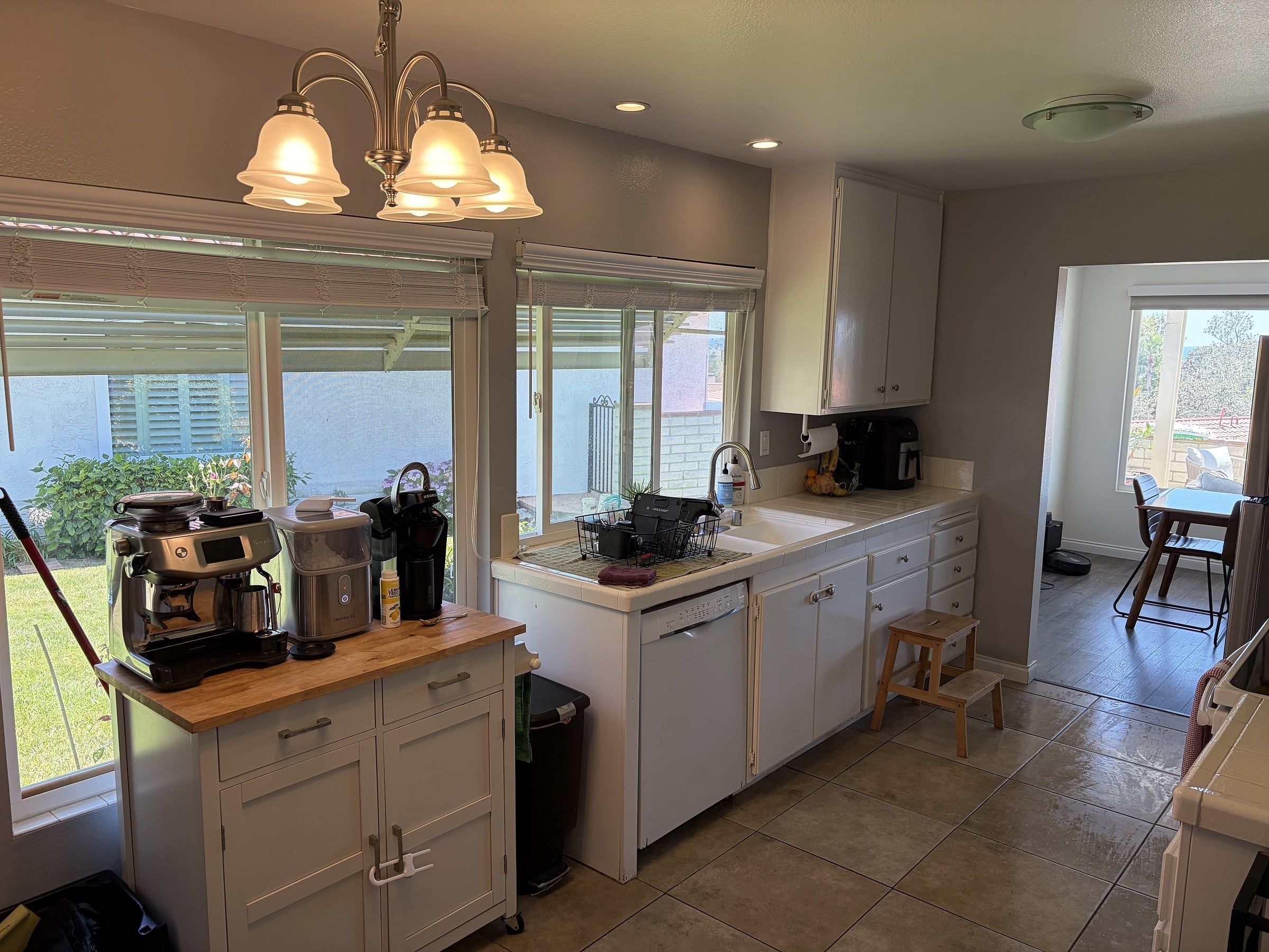 Kitchen with white cabinets, butcher-block island holding a espresso machine, white dishwasher, sink, and a chandelier overhead