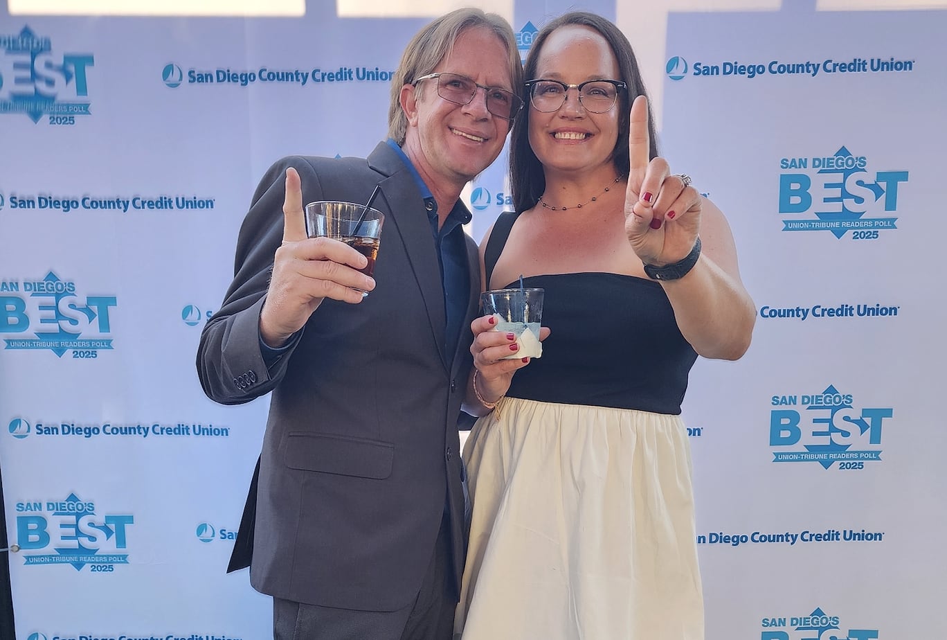 Two people holding drinks and making number 1 signs in front of a "San Diego's Best 2025" step-and-repeat banner